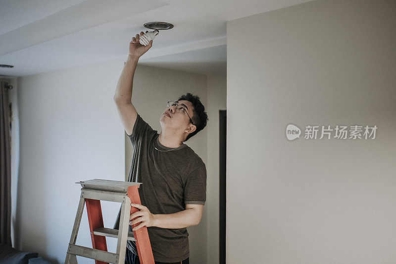 an asian chinese mid adult male changing light bulb in living room, apartment home